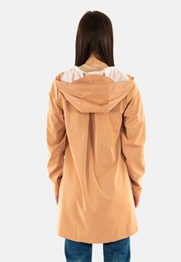 Giacca impermeabile beige con cappuccio, dotata di un rivestimento bianco a contrasto, polsini elasticizzati e una vestibilità rilassata, che arriva sotto ai fianchi.