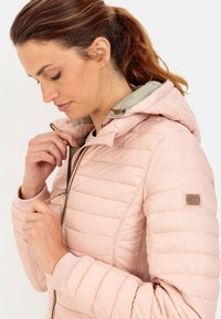 Rosa isoleret jakke med quiltet tekstur, lynlåslukning foran og hætte. Har en kontrasterende lys indvendig foring og et logo-patch på ærmet.