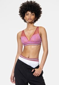 Bra features translucent pink lace and a deep V design with red accents. Paired with dark pants, showcasing an elastic waistband.