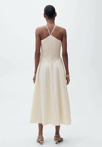 Cremfarbendes Midi-Kleid mit strukturiertem Oberteil und verstellbaren Spaghettiträgern, ausgestattet mit einem ausladenden Rock und einem glatten, leichten Stoff.