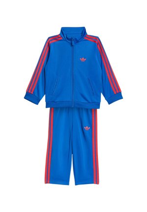 Blåt todelt træningssæt med røde striber på ærmer og bukseben, lynlåstrøje og Adidas-logo på bryst og bukser.