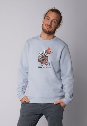 Lichtblauwe sweater van zachte stof met een beerafbeelding in gestreepteoutfit en een rode hoed, vergezeld van de tekst "Pour de Franz."