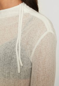 Hanorac alb cu glugă, realizat dintr-un material texturat și transparent, având un design gradient care trece de la gri la piersică. Cordonas la gât.
