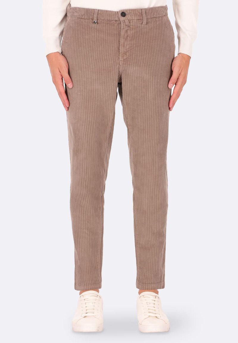 Pantaloni in velluto a coste marroni con righe verticali, slim fit e chiusura con bottone. Abbinati a sneakers bianche.