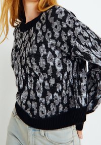 Stickad tröja med ett leopardmönster i grå och svarta nyanser. Har en ribbad halsringning och fåll. Tillverkad av textilmaterial.