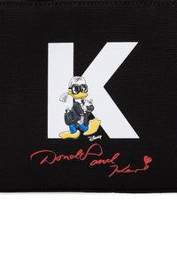 Schwarzes Stofftäschchen mit einem großen weißen Buchstaben "K" und einer Cartoon-Ente in einem stylischen Outfit. Unten befindet sich roter Signaturtext.