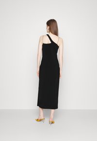 Černé midi šaty s asymetrickým designem ramínka, hladkou texturou a přiléhavým střihem. Spárované s žlutými sandály na podpatku.