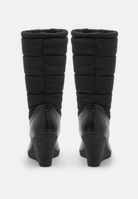 Bottes noires montant jusqu'au genou avec une tige en nylon matelassé et un talon compensé texturé ; éléments en cuir lisse sur les côtés et à l'arrière.