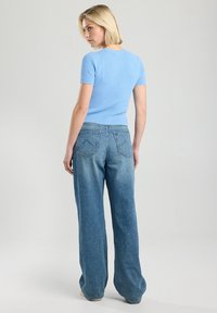 Light blue, ribbed knit short-sleeve top paired with loose, faded blue jeans, featuring a classic five-pocket design and visible stitching accents.