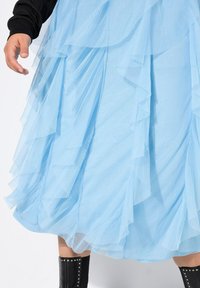 Gonna in tulle azzurro chiaro con strati di balze. Il tessuto appare morbido e leggero, messo in risalto da una maglia nera e stivali al ginocchio con borchie.