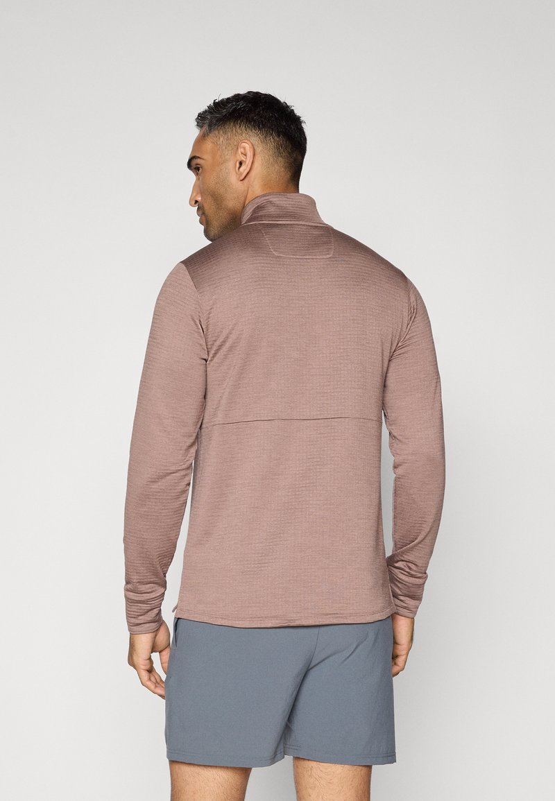 Langærmet pullover i en afdæmpet rosenfarve, med en lynlåskrage og ribbet tekstur. Sammenstykket med grå shorts, der viser en tætsiddende silhuet.