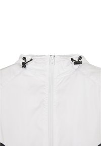 Vit jacka med dragkedja, justerbara svarta knappar och texturerat tyg. Designen inkluderar huva och raglanärmar.