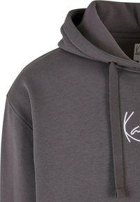 Grå hettegenser med snor, laget av et strukturert stoff og med hvitt brodert logo på fronten. Enkelt og uformelt design.
