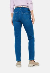 Jean en denim bleu avec une coupe droite, des poches arrière et une taille basse. Assorti avec des chaussures à plateforme beiges, présentant un design texturé.