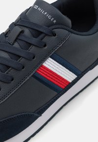 Sneaker in pelle blu marina con superficie texturizzata, dettagli a strisce blu e rosse in contrasto, e particolari bianchi, dotata di chiusura con lacci e logo.
