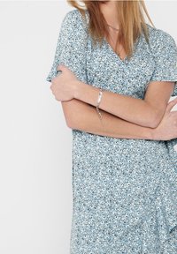 Robe enveloppante bleu clair présentant un motif floral avec des accents blancs et noirs, des manches courtes et une texture douce et fluide.