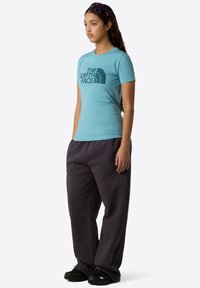 Lyseblå kortærmet t-shirt med sort grafisk logo, parret med mørkegrå sweatpants. Model iført sorte sneakers.