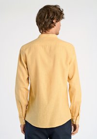 Maglietta a maniche lunghe in tessuto giallo chiaro, con colletto, polsini con bottoni e orlo a forma curva. Design testurizzato e informale.