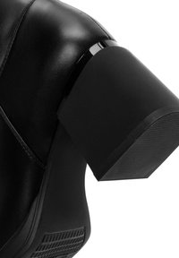 Bottine en cuir noir avec un talon épais noir mat à surface texturée, et des coutures élégantes le long du côté.