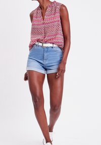 Haut sans manches rose et blanc à motifs, associé à un short en denim bleu taille haute avec des ourlets retroussés. Accessoirisé d'une ceinture blanche.