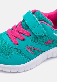 Chaussure de sport turquoise avec un tissu en maille, des accents roses et une lanière Velcro. Elle possède une semelle blanche et des détails texturés sur le dessus.