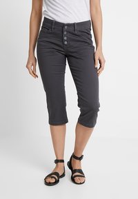 Pantalons gris coupés avec un devant à cinq boutons et un design ajusté. Associés à des sandales noires à lanières.