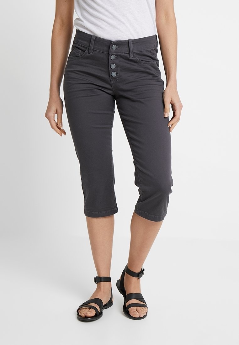 Pantalons gris coupés avec un devant à cinq boutons et un design ajusté. Associés à des sandales noires à lanières.