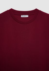 T-shirt in cotone color bordeaux con scollo rotondo e maniche corte. Presenta una texture liscia e un'etichetta con la scritta "CALLIOPE" in un piccolo tag.