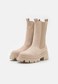 Beige ankle boots mit einer glatten Lederaußenseite, elastischen Seitenpanelen und robusten Gummisohlen mit einem gerippten Muster.