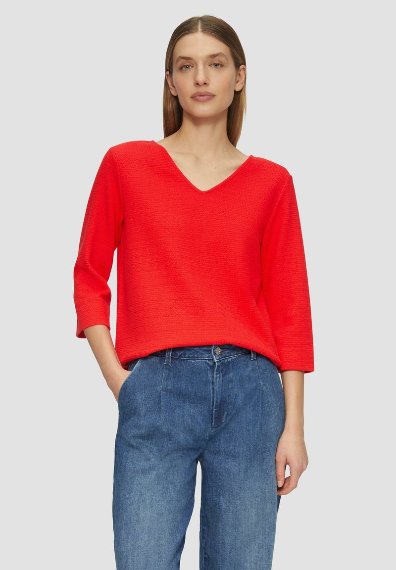 Maglione rosso, testurizzato, con scollatura a V e maniche a tre quarti, abbinato a jeans in denim azzurro chiaro, morbidi e comodi.