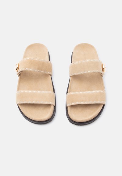 Μπεζ σουέντ σανδάλια τύπου σλάιντ με δύο φαρδιές λουριά που έχουν λευκά ράμματα και μια μικρή χρυσή αγκράφα στο πάνω λουρί, μαύρες σόλες.