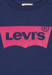 Mornarska dukserica s velikim ružičastim Levi's logotipom; ima okrugli izrez i rebraste rukave. Glatka tekstura s tiskanim grafikom.