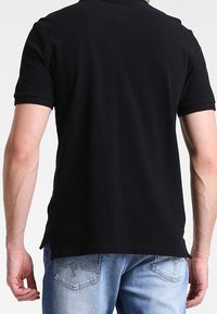 Polo shirt noir à manches courtes en coton avec une texture lisse. Doté d'un col classique et d'un ourlet arrière légèrement plus long.