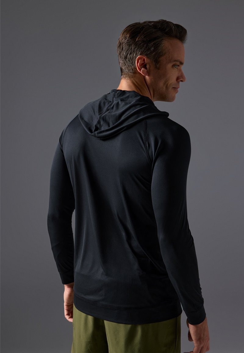 Czarna, długorękawowa koszulka z kapturem, wykonana z gładkiego materiału, o luźnym kroju i prążkowanej strukturze, zestawiona z jasnoszarymi szortami.