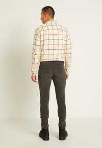 Camisa branca xadrez com linhas laranja e azul-marinho, combinada com calças justas cinza-escuras e botas de tornozelo pretas. Design simples e funcional.