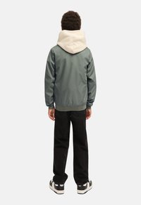 Šedá lehká bunda s krémovou kapucí, spárovaná s černými džíny a teniskami, ukazuje jednoduchý, sportovní design bez ozdob.