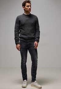 Suéter gris de punto con cuello acanalado, combinado con jeans slim fit gris oscuro y zapatillas blancas con acentos verdes. Diseño simple y texturizado.