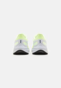 Une paire de chaussures de sport jaune fluo et blanche vues de l'arrière sur un fond blanc uni.
