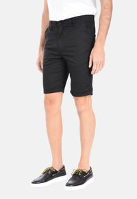 Pantaloni neri fino al ginocchio realizzati in tessuto morbido con taglio dritto, dotati di orli arrotolati e tasche laterali. Abbinati a scarpe in pelle nere.