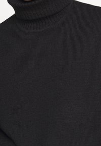 Schwarzer Rollkragenpullover aus geripptem Strickmaterial, mit hohem Kragen und körpernahem Schnitt. Weiche Textur mit minimalistischen Details.