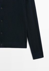 Mörkblå kofta i mjukt stickat material. Har knäppning framtill, långa ärmar och ribbad nederkant och manschetter. Inga mönster eller accenter.