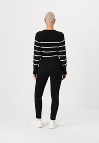 Zwart-wit gestreepte gebreide trui met een ronde hals, gecombineerd met zwarte skinny jeans en witte sneakers, gezien vanuit de achterkant.