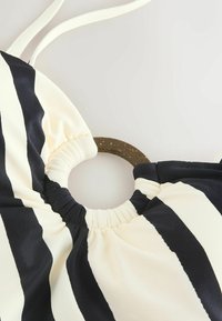 Haut de bikini rayé noir et crème avec un accent circulaire marron, featuring une matière froncée au niveau du décolleté et des bretelles ajustables.