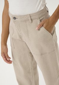 Beige and white striped pants made of cotton, featuring a front button, side pockets, and a relaxed fit.