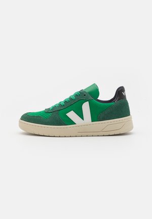 Grüne Wildleder-Sneaker mit weißem V-Logo, perforierter Zehenpartie und beiger Gummisohle. Ausgestattet mit grünen Schnürsenkeln und einem dunkelblauen Rückenteil.