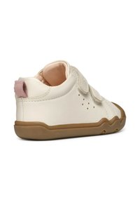 Zapato blanco de cuero con suela de goma marrón, correa de velcro y acento rosa en el talón. Cuenta con pequeñas perforaciones para ventilación.