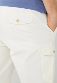 Pantaloni cargo bianchi con due tasche posteriori dotate di chiusura a bottone. Il tessuto appare liscio, con una vestibilità rilassata e orli ripiegati.