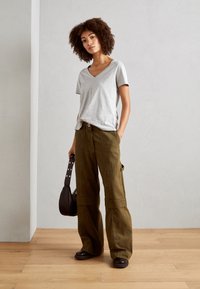 Gray short-sleeve V-neck t-shirt, olive green wide-leg cargo pants, black rounded shoes, and a small dark shoulder bag. Wood floor background.