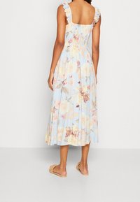 Vaaleansininen kukkakuosisesti midi-mekko, jossa on laskostetut hihnat, napakka yläosa ja virtaava hame. Mekossa on ruusu- ja lehtiote pehmeissä pastellisävyissä.