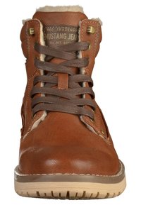 Bruna läderankelboots med en texturerad finish, försedd med bruna snören, gyllene öglor och en krämfärgad pälsfoder vid toppen.